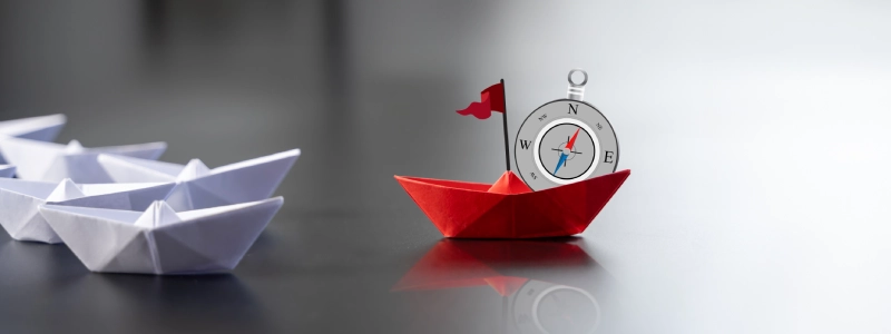 Red origami boat leading a group of white boats, illustrating vision, direction, and creative distinction.