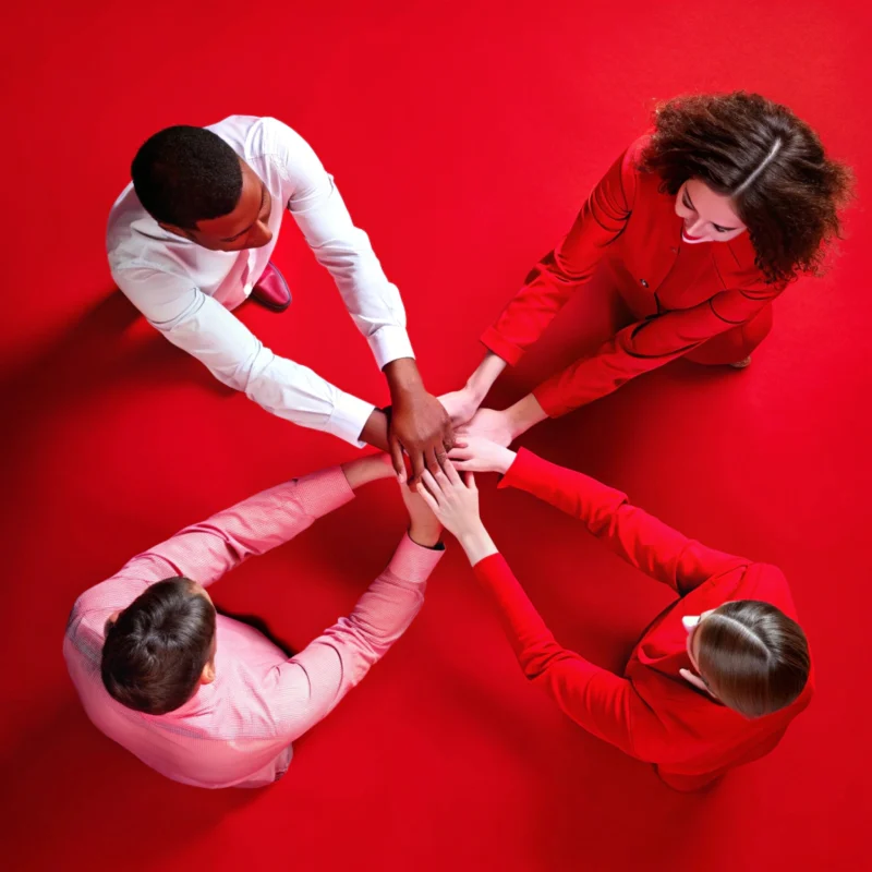 Group of four people joining hands to represent teamwork, trust, and collaboration.